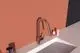 Küchenarmatur von Ideal Standard in Rosé mit einem gebogenen Auslauf und Bedienhebel. Auf einem hellen countertop vor einer rötlichen Wand platziert.